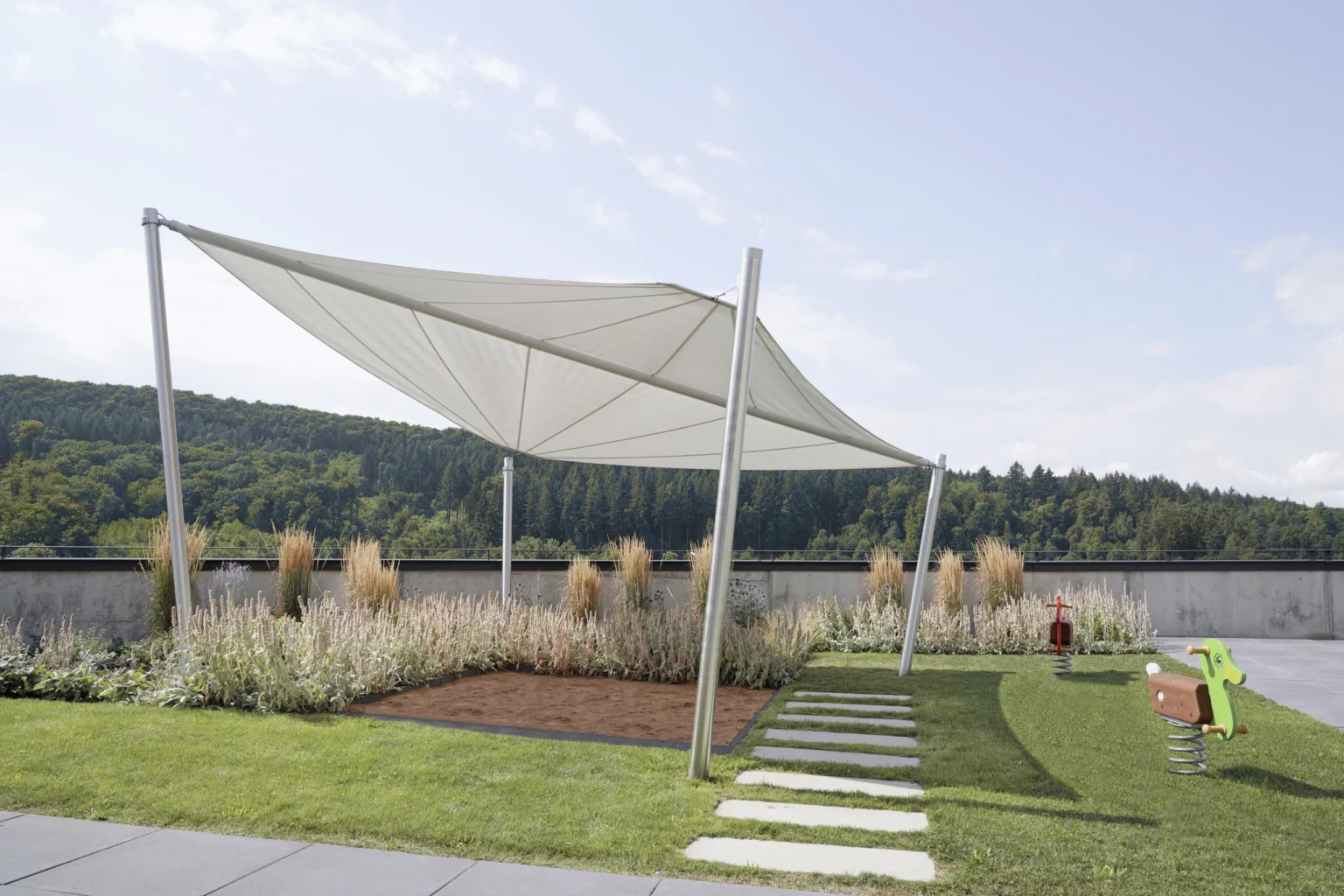 Moderne Sonnensegel über einem Spielbereich mit grüner Landschaft im Hintergrund