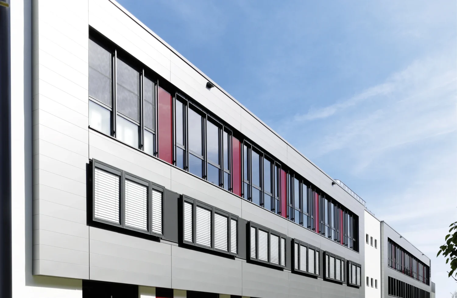 Modernes Schulgebäude mit grauen und roten Fassadenelementen bei klarem Himmel